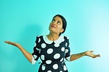 A girl in a polka dot dress looking up with her hands out in a questioning shrug