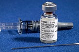 Close-up photo of three components of a smallpox vaccination kit with the vial of vaccine in the foreground on a blue background
