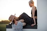 Young hip-looking couple talking. He’s in stylish hat and she has short cropped platinum blonde hair.