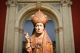 A sculture of a bishop stands in a doorway with a dour expression.