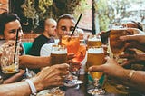 Glasses of beer and alcoholic drinks being clinked in a cheers at an outside table