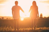 A man and a woman holding hands with the sunset in the backdrop
