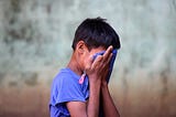 An emotional moment captured of a boy covering his face with his shirt and hands. (Photo by Lucas Metz on Unsplash)