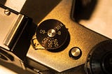 Close up monochrome photograph of the top plate of a camera showing the shutter speed selection dial.