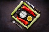 A square made of four pawpaw stocks, in which there are two chili peppers, a slice of orange, and a small clock