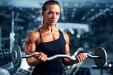 A very fit female bodybuilder smiles as she performs curls, showing amazing upper body development.