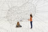 Two children play in an interconnected web of threads creating two colliding spheres with their interscetions.