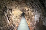 Long stretch of sewer under Cleveland. Brick lined and built in 1873 it is still in use today. Brick is rounded and very weathered but intact. walls are lined with white mineral deposits and a stream of discolored water is flowing down the bottom middle of the pipe. photo credit Matt Barker, Cody Kelley, and Damien Csiszar.