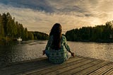 Image contains a lady sitting on a dock at peace