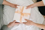 A couple holding a white gift box with a pink ribbon