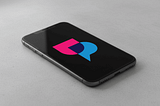 UpScrolled logo in pink and blue speech bubble design on smartphone screen against neutral gray background.