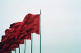 Five red flags blowing left on flagpoles.