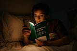 A person reading the book ‘Considerate Content’ by Rebekah Barry in bed by the light of a mobile phone.