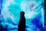 Anadol standing in front of one of his works. A screen displaying blue and turquoise light nodes.