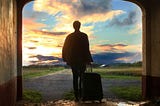 The silhouette of a man walking, dragging a wheeled suitcase behind him