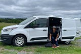 Rene Cizio sits in her white Ford Transit Connect van putting on her hiking boots.