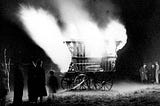 1920s archival back & white photograph of a Gypsy/Traveler’s caravan ablazed — Traditional funeral ceremony.