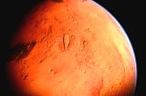 A close-up view of the red planet Mars, showing its rocky terrain and glowing orange atmosphere.