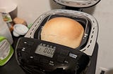 Bread maker, with door open, revealing a freshly-baked loaf in the pan.
