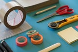 Tape, rotary cutter, notes, and scissors on a blue desktop