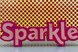 Pink sign that says “Sparkle” against a yellow backdrop with pink polkadots.