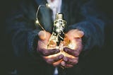 A person holding an illuminated light bulb.