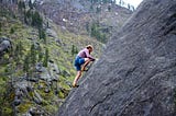 Man climbing rock face, with safety rope belay connection.