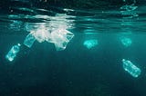 Resíduos plásticos flutuando e submersos no oceano, incluindo garrafas e sacolas transparentes, evidenciando a poluição marinha em águas azul-esverdeadas