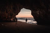 Man standing in front of a beach cave entrance