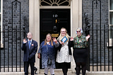 Members of the My Vote My Voice accessible voting coalition hand in #MyVoteMatters petition to Downing Street, 26th July — One man and three women stand infront of Downing Street waving their hands, one holds a box with My Vote My Voice logo on it.