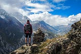 man on a hike in front of a stone pile, maybe a grave, in the mountains. What do you control?