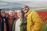 A group of friends smiling with autumn coats in front of a poppy field.
