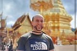 A photograph of me candidly smiling. Behind me is the famous giant gold pagoda found at Wat Phra That Doi Suthep (temple).