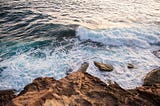 Colour image of rocks at a cliff base and ocean waves crashing onto them