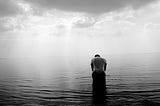 solitary figure bows his head in a body of water