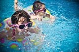 Two little girls in a swimming pool, with inner tubes and pink sunglasses