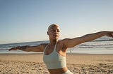 A Black woman with a blonde, short cut does yoga on the beach.