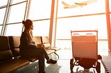 A woman waits in an airport while watching a plane take off