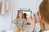A mother photographs her smiling daughter indoors, capturing a joyful moment.