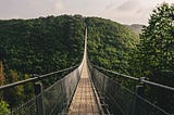 long, scary, narrow wooden bridge over a valley through lush mountains.