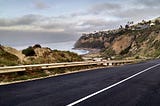 Color photo of road leading down to the Pacific Ocean cloudy sky above ocean and bluffs of Palos Verdes Peninsula in the background to the right Stella Martann copyright 2019.