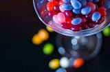 Colourful candy beans falling out of a glass utensil
