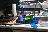 A sink and counter full of dirty dishes that are still molding in the author’s house.