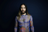 Jared Leto in a mesh top, looking into the camera