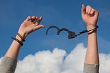 Image of woman’s hands with a broken handcuff.