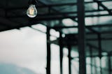 Dim light hanging in glass structure, with view of overcast sky.