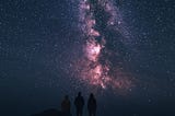 A starry night sky with a silhouette of 3 people stargazing