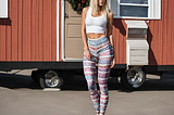 A woman, dressed in a crop top and leggings, stands outside a mobile home.
