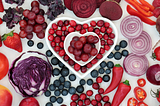Blue, red and purple fruits and vegetables arranged into art forming a heart.