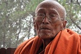 Picture of an old Buddhist monk with weathered face and an orange robe draped over his shoulder